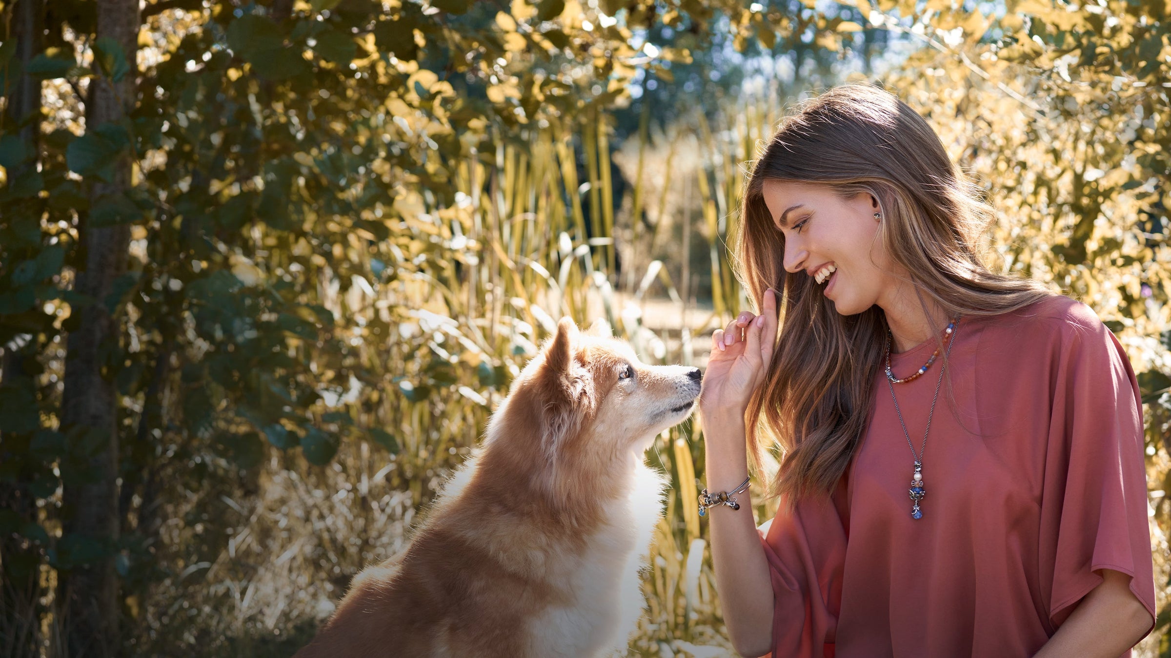 Woman playing with her dog in nature wearing Trollbeads jewellery from the love off Paws collection